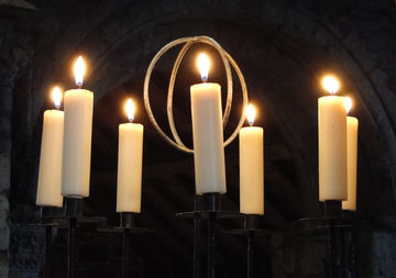 Kerzenhalter mit mehreren brennenden Kerzen in einem abgedunkeltem Kirchenraum