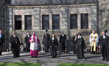 Pfarrer verschiedener Konfessionen stehen vor einer Kirche.